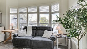 Een woonkamer met een zwarte leren bank, een ronde houten tafel en een potplant.