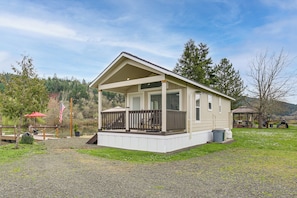 A single-story cabin with a porch, a covered outdoor seating area, and a dock extending into a body of water.
