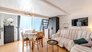 Ein modernes Wohnzimmer mit Essbereich, einer Couch, einem Fernseher und einem Bücherregal.