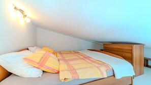 Ein Schlafzimmer mit einem Bett, Kissen, einer Holzkommode und einer Wandleuchte.