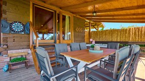 Un espace extérieur abrité, avec une table et des chaises en bois, un jeu de fléchettes et un panneau d’accueil.
