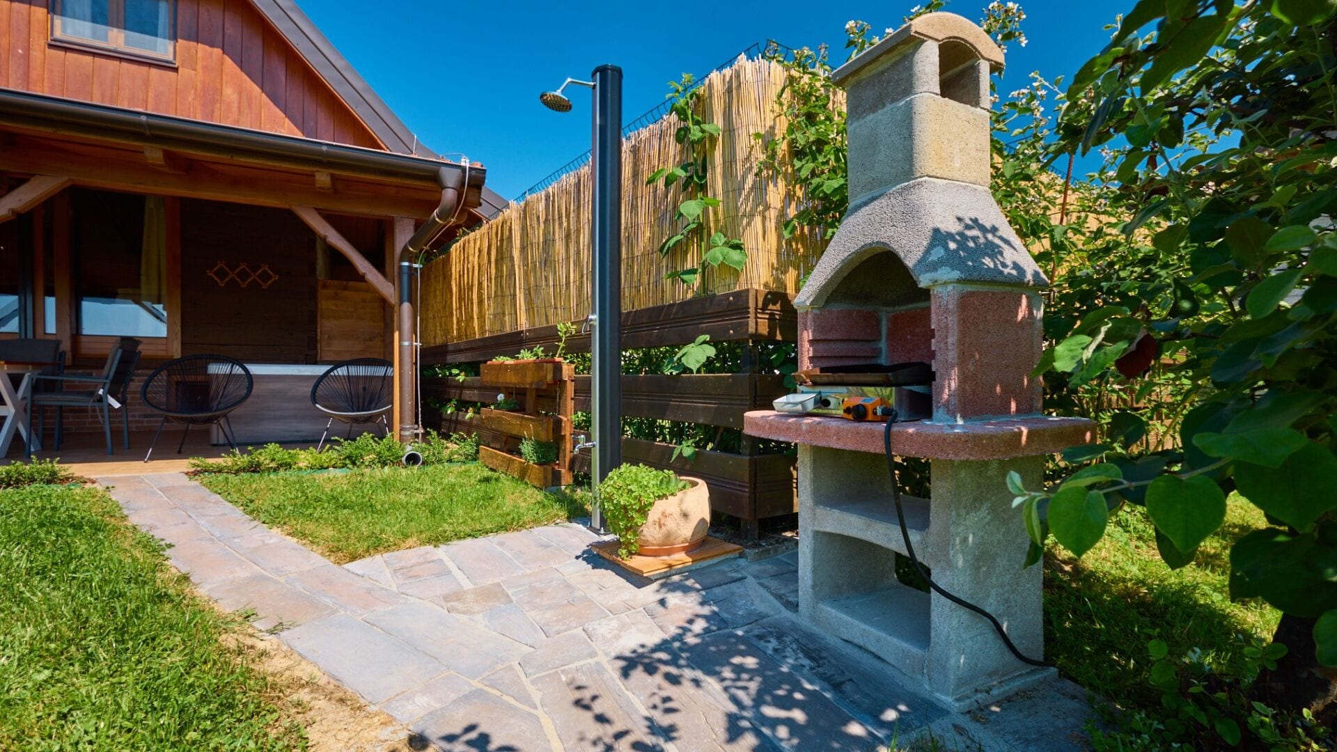 Una cabaña de madera con una parrilla de piedra, una cerca de madera y un patio con mobiliario exterior.
