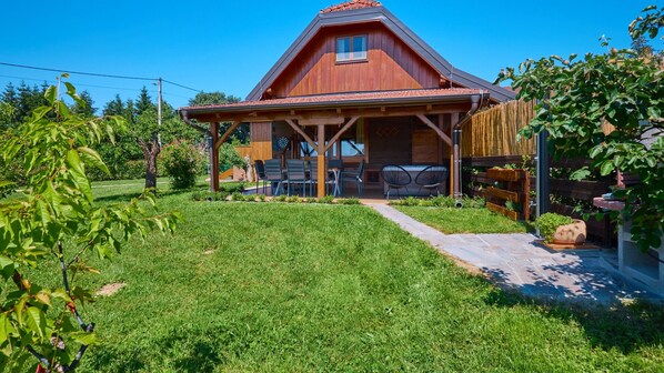 A wooden house with a covered patio, outdoor seating, and a well-maintained lawn.
