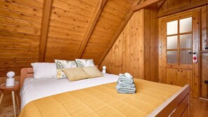 Ein gemütlicher Holzraum mit Bett, Kissen, einem Nachttisch und einer Tür mit satinierten Glasscheiben.