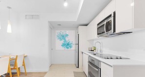 A modern kitchen with white cabinetry, a stainless steel refrigerator, a microwave, and a gas stove. - Marina Front - 2BR - Beachwalk Resort (Hallandale Beach)