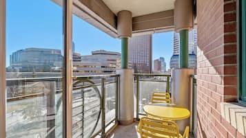 A balcony with a glass railing, yellow chairs, and a table.