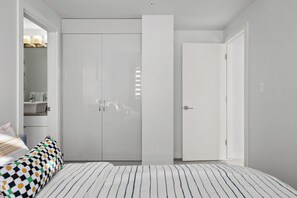 A bedroom with a bed, a wardrobe, and a door leading to another room. - 2 Bed, 2 Bath Condo in the Heart of Downtown Calgary Near Saddledome & Stampede (Calgary)