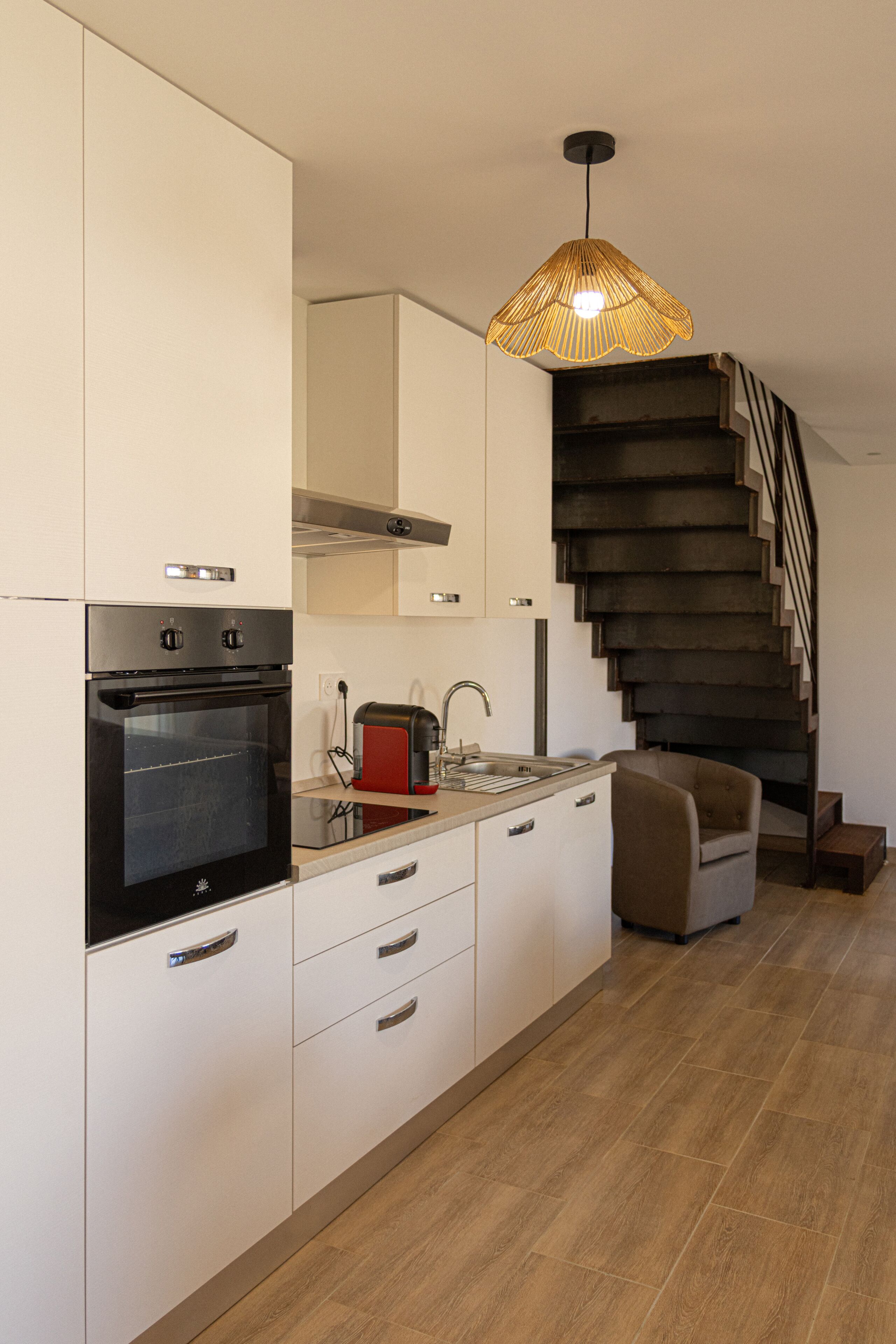 Una cocina moderna con horno empotrado, tostadora y pileta. Se ve una escalera que sube a un nivel superior.