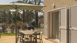 Een terras buiten met een tafel, stoelen, een zonnescherm en een gebouw met luiken.