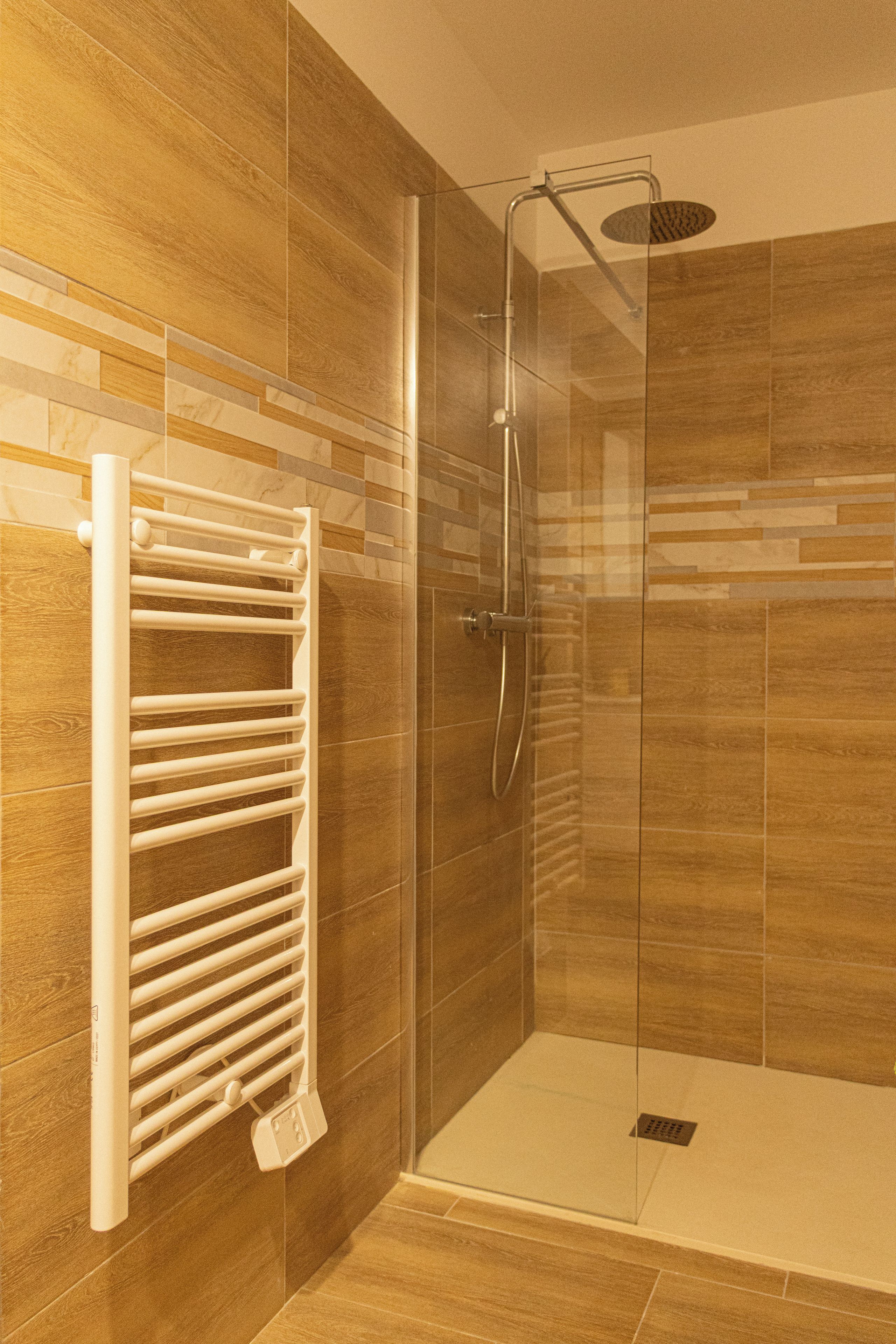 A shower area with a glass door, a white towel rack, and tiled walls.