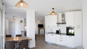 Een moderne keuken met witte kasten, een inbouwoven en een eethoek met een houten tafel en stoelen.