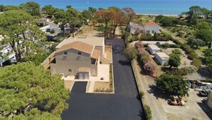 Luchtbeeld van een woongebied met een opvallend huis op de voorgrond, omringd door bomen en een helder uitzicht op de zee.