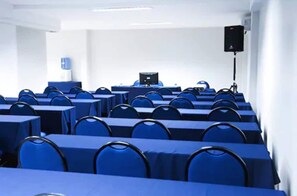 Une salle de conférence avec des rangées de tables et de chaises, un projecteur et un système audio.