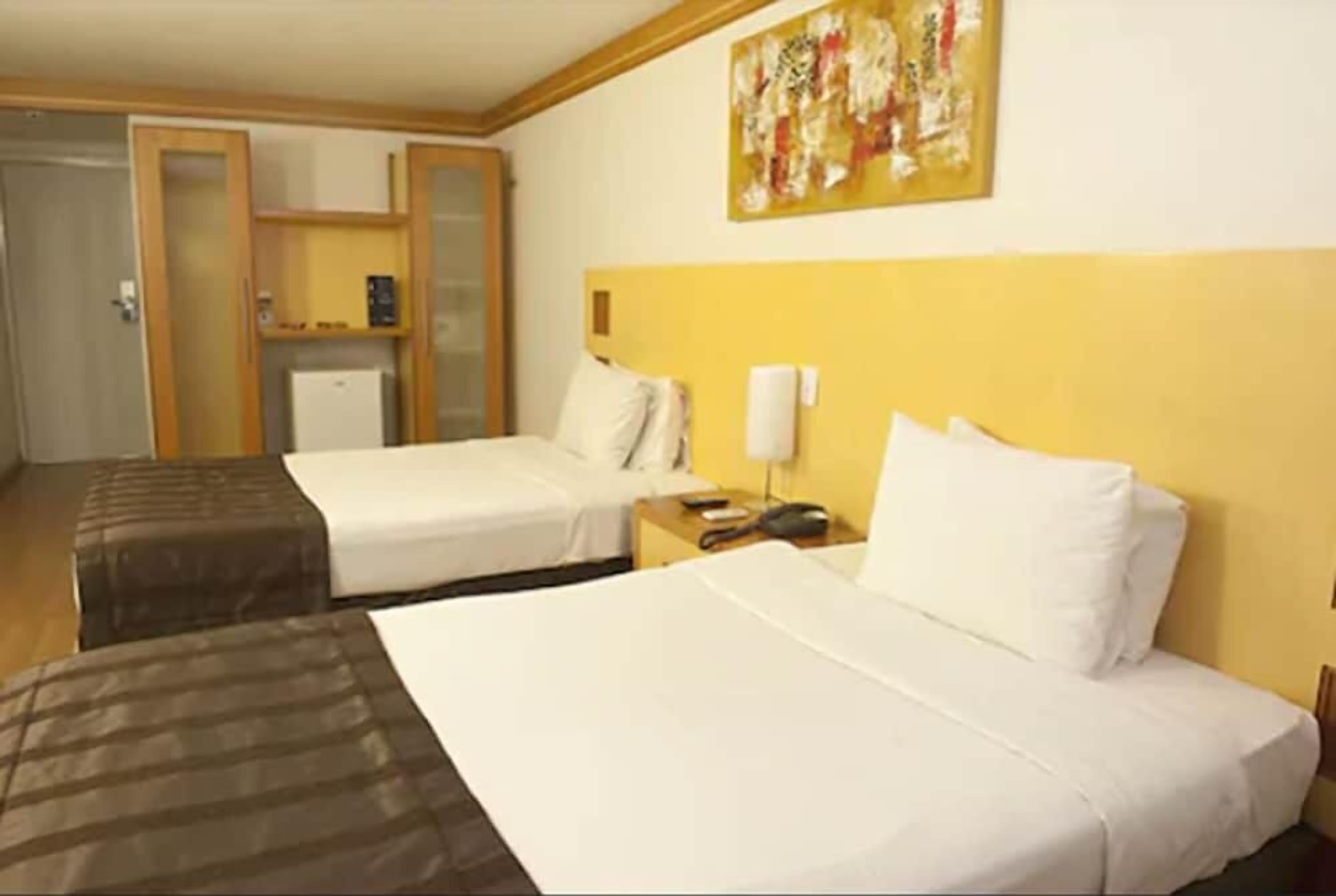 A hotel room with two beds, a small desk, a telephone, and a wall-mounted artwork.