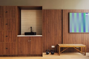 A room with a wooden cabinet, a small shelf with a black electronic device, a bench, and two kettlebells. - Habyt Vienna (Vienna)