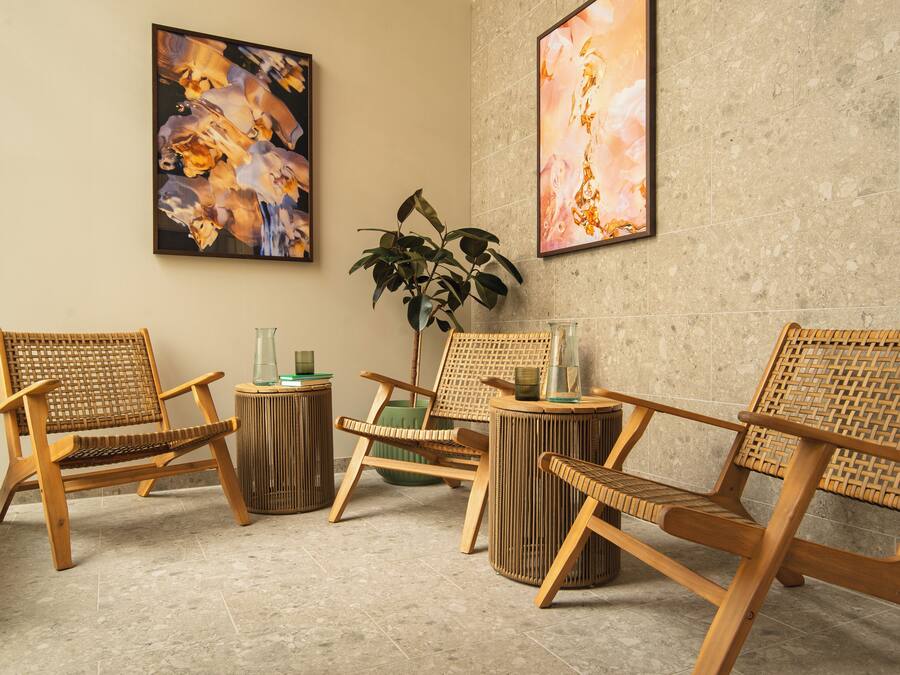Ein Zimmer mit vier Holzsesseln, einer grünen Pflanze und zwei abstrakten Bildern an der Wand.