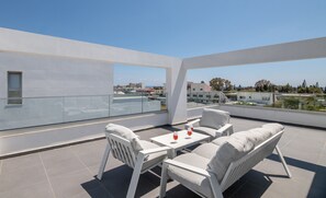 Eine Dachterrasse mit weißem Tisch und Stühlen, einem kleinen Fenster und Blick auf die Stadtlandschaft.