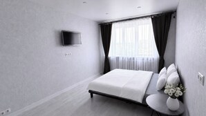 Ein modernes Hotelzimmer mit einem Bett, einem Flachbildfernseher, einem Fenster mit Vorhängen und einem kleinen Tisch mit einer Blumenvase.