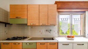 A kitchen with wooden cabinets, a gas stove, a sink, and a window with a view of greenery. - Holiday Home 'Casa Al Mare 482' with Shared Garden, Wi-Fi and Air Conditioning (Frassanito)
