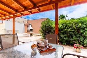 Eine Terrasse im Freien mit einem Glastisch, gedeckt für ein Frühstück, einem Grill und einem Stuhl.