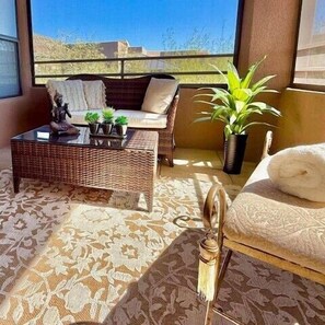 A balcony with a wicker sofa, a small table with plants, a potted plant, and a chair with a towel. - Spectacular City View from Picture Window and Mountains from screened Patio (Tucson)