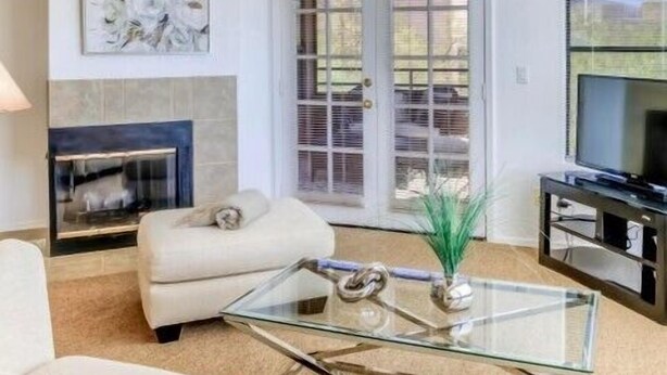 Una sala de estar con chimenea, un sofá, una mesa de centro de vidrio, un televisor y una puerta que da al exterior.