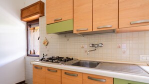 Una cocina con armarios de madera, una estufa a gas, un fregadero y una ventana con cortina.