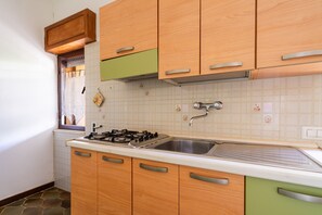Eine Küche mit Holzschränken, einem Gasherd, einer Spüle und einem Fenster mit Vorhang.