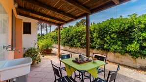 Un patio al aire libre con una mesa lista para comer, rodeada de sillas y un lavamanos a la izquierda.