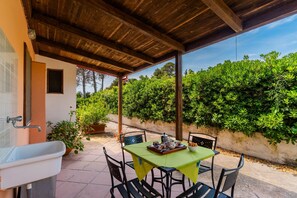 Eine Terrasse im Freien mit einem für das Essen gedeckten Tisch, umgeben von Stühlen und einem Spülbecken links.