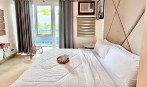 Um quarto com cama, mesa de cabeceira, cadeira, janela com cortinas e vista para o exterior.