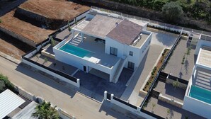 Ein modernes, zweistöckiges Haus mit Pool auf dem Dach, gepflasterter Auffahrt und angelegtem Garten.