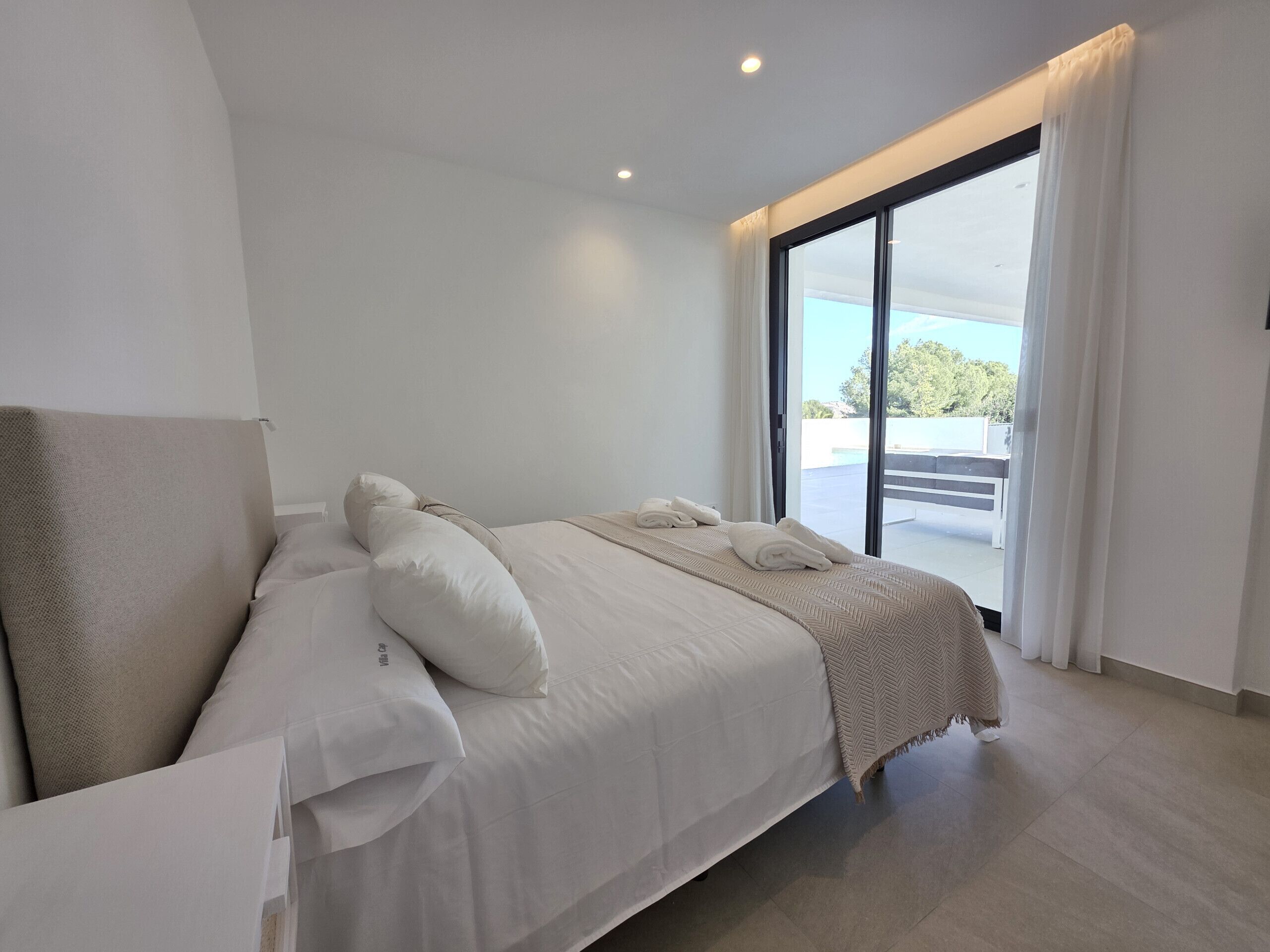 A modern hotel room with a large bed, a view of the outdoors, and a balcony.