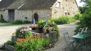 A stone building with a gravel driveway, a garden with flowers and plants, and outdoor furniture.