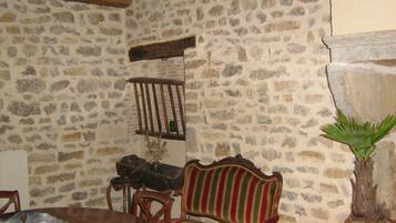 Une pièce aux murs de pierre, avec une table à manger en bois, une chaise à rayures, une plante en pot et une étagère sur laquelle se trouve une bouteille.