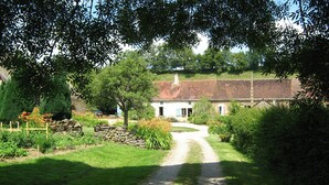 Ein ländlicher Pfad führt zu einem traditionellen Haus mit Steinmauer und Garten.