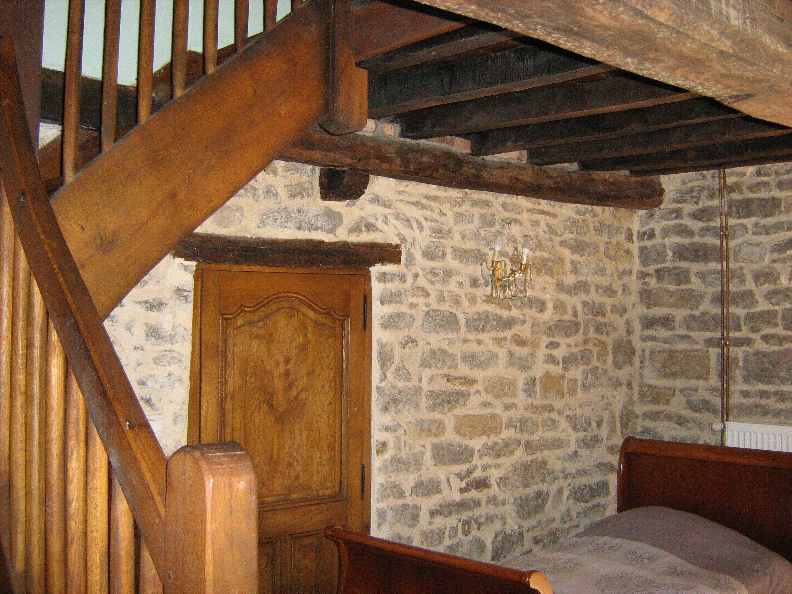 Une chambre avec un escalier en bois, un mur en pierre, une porte en bois et un lit.