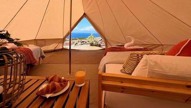A tent with a bed, a table with a croissant and juice, and a view of the ocean. - The Treehouse Surf Camp (Hoya Grande)