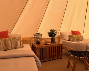 A tent interior with two beds, a small table with a plant, a lantern, and a chair. - The Treehouse Surf Camp (Hoya Grande)