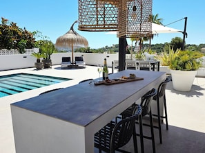 An outdoor terrace with a pool, a dining area with chairs and a table, and a decorative umbrella.