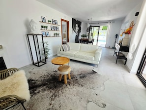 En moderne stue med en hvid sofa, et rundt træbord, en sort-hvid måtte og en væg dekoreret med billeder og planter.