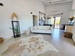 A spacious living area with a white sofa, a large rug, and a dining table.