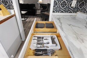 Une cuisine dotée d’un plan de travail en marbre, d’un organiseur en bois pour les tiroirs contenant des ustensiles, et d’un crédence décorée.