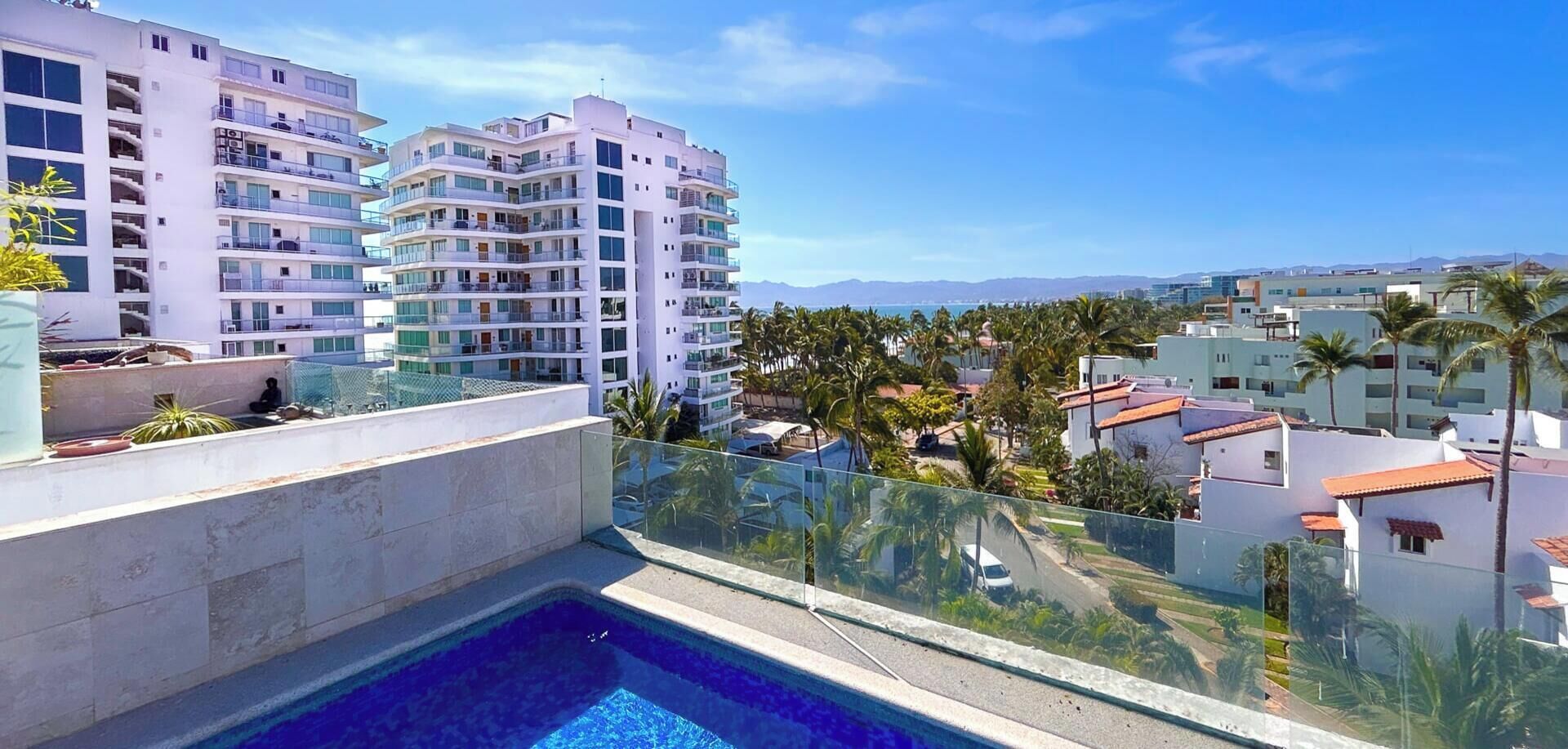 Piscina no terraço com vista clara para edifícios e palmeiras ao redor.