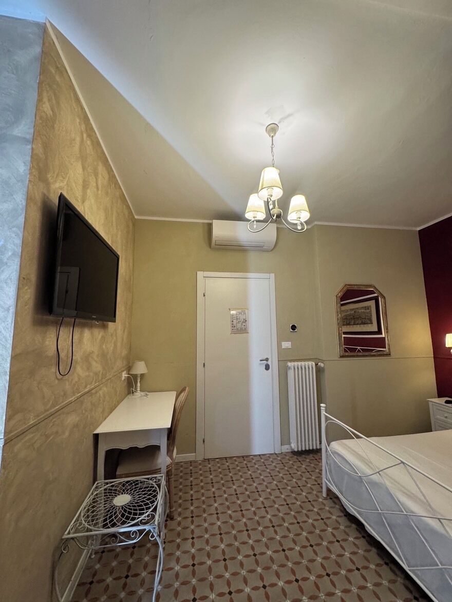 Een slaapkamer met een bed, een bureau met stoel, een televisie, een radiator en een plafondlamp.