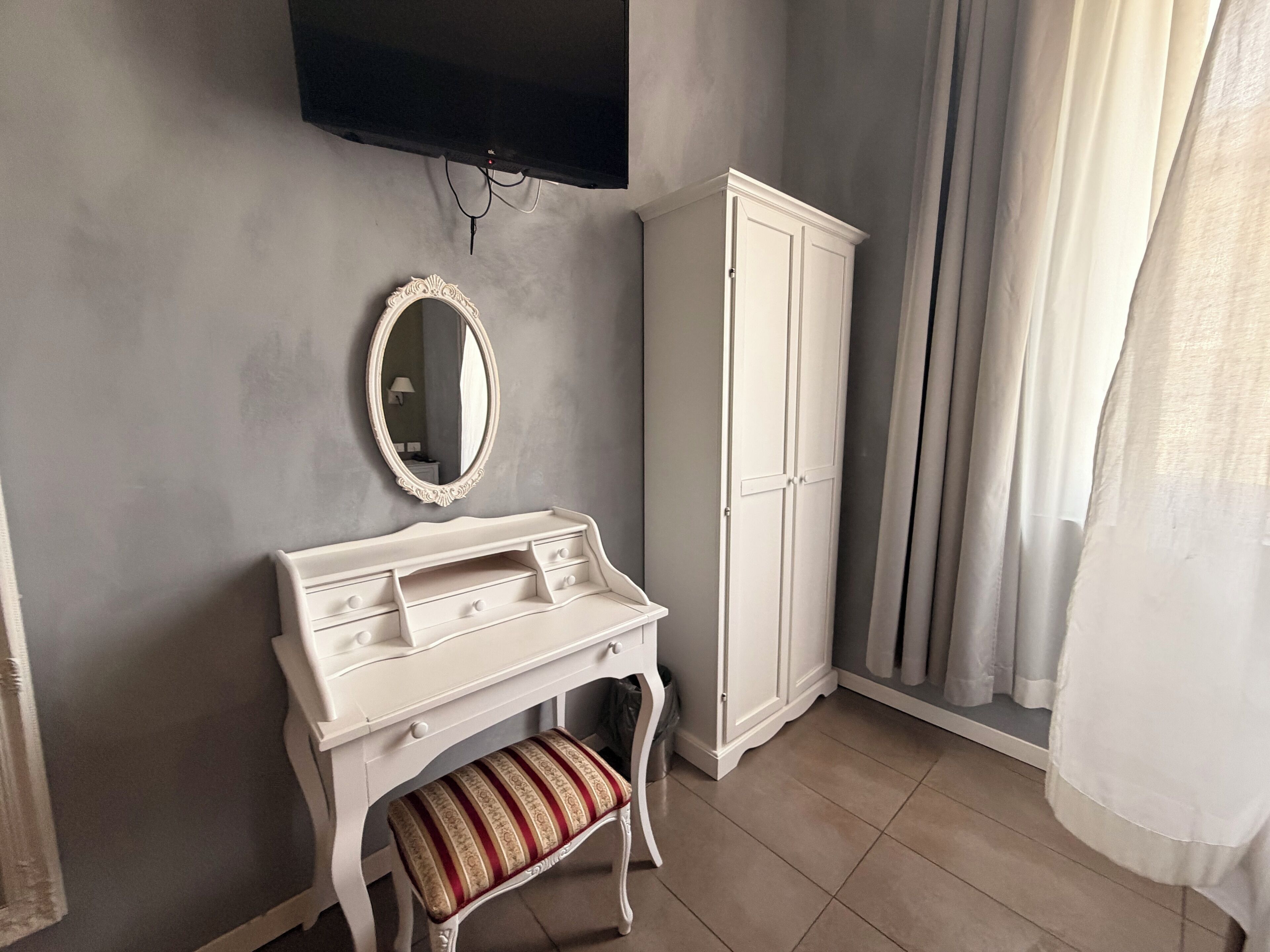 A room with a vanity, a mirror, a cabinet, and a television mounted on the wall.