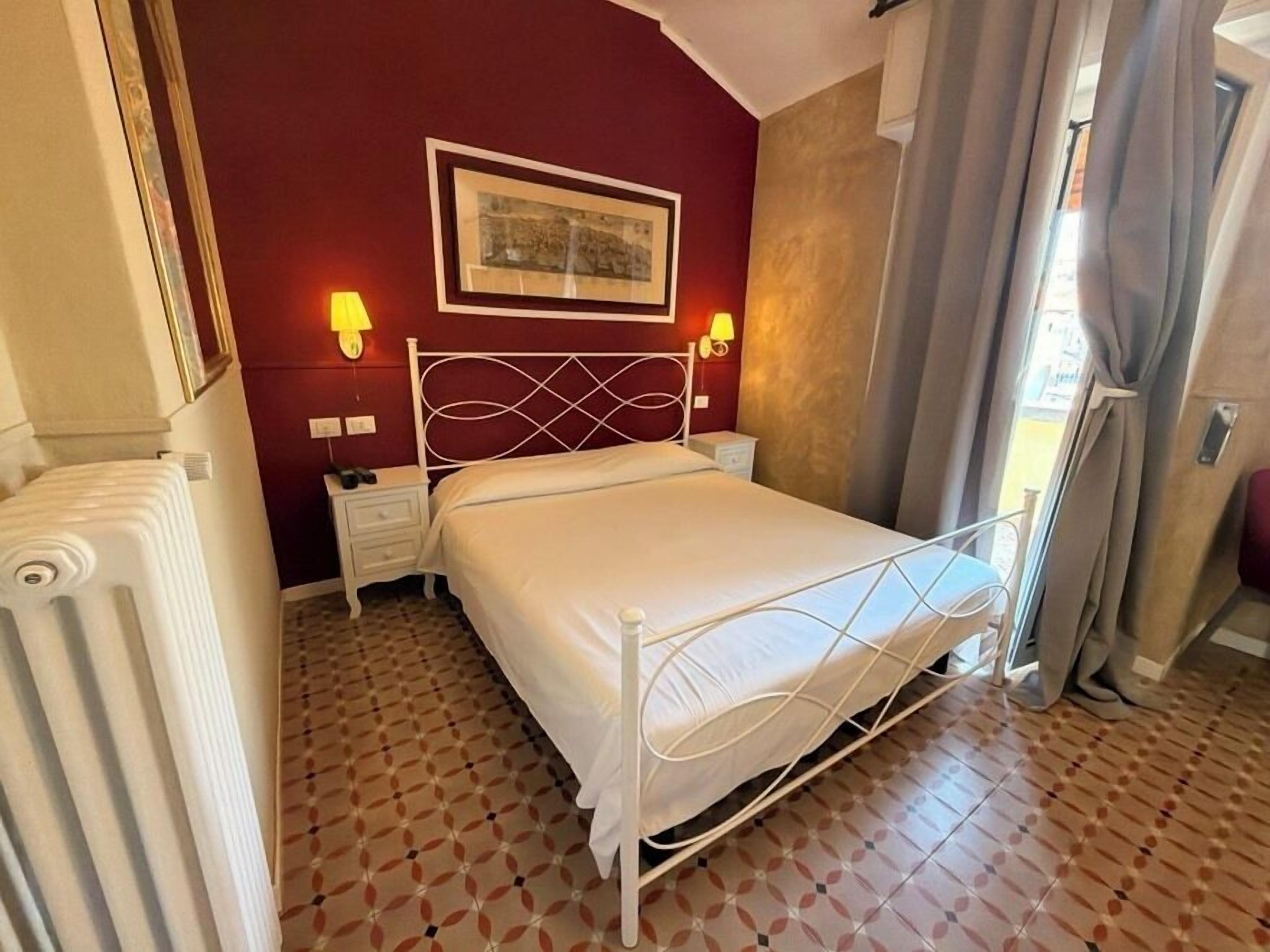 A bedroom with a bed, nightstands, a lamp, a radiator, and a patterned floor.