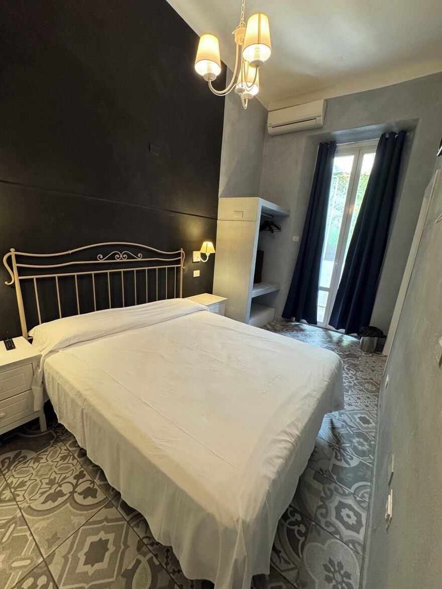 Une chambre à coucher comprenant un lit, des tables de chevet, un lustre, un appareil de climatisation et un sol à motifs.