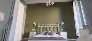 A bedroom with a metal bed frame, two bedside tables with lamps, a window with blinds, and a chandelier. - Boutique Hotel Washington Milano (Milan)