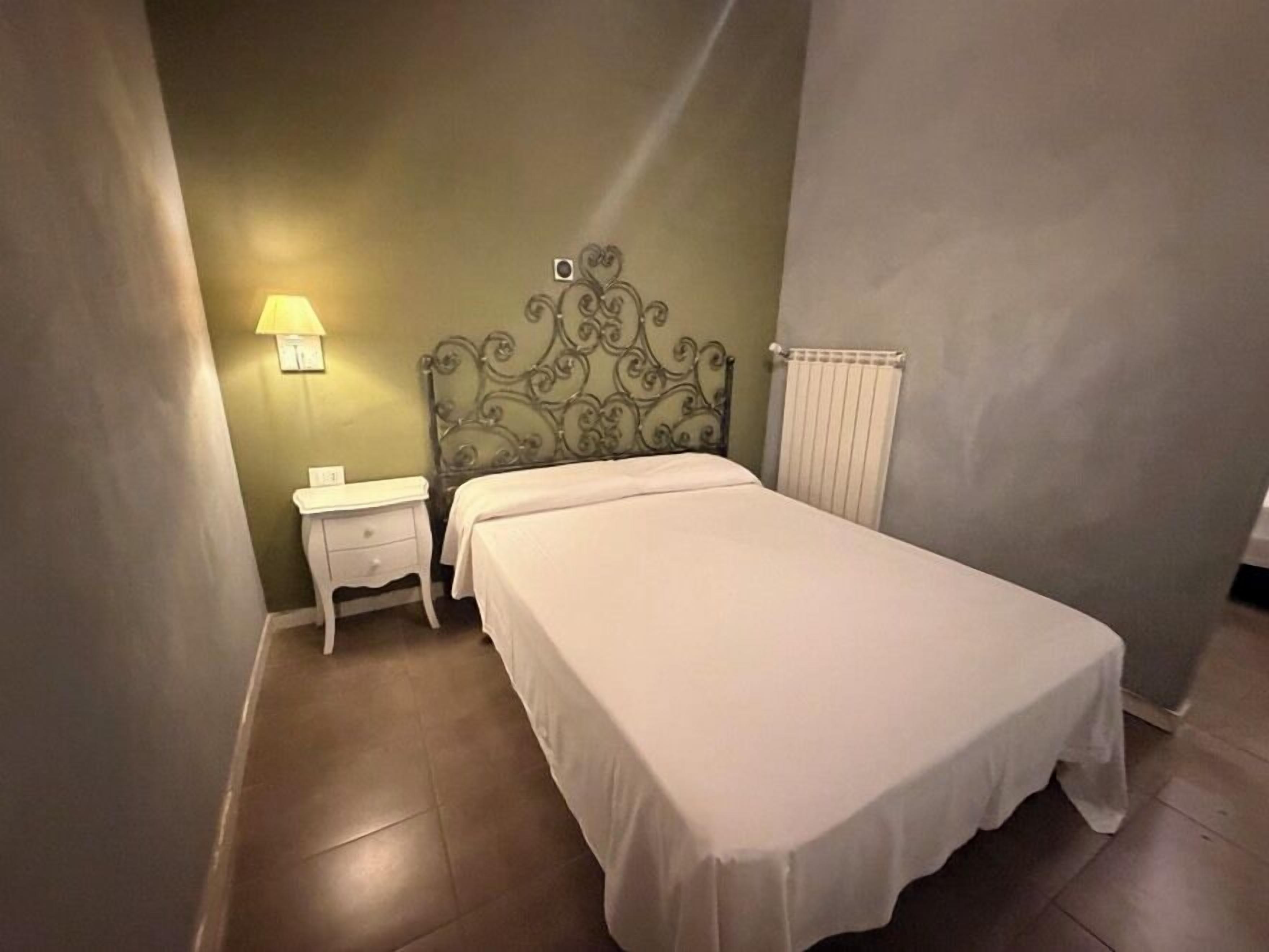 Un dormitorio con cama, mesita de noche, lámpara y radiador.